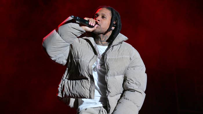 Durk with long braids, wearing a puffy jacket, performs on stage while holding a microphone. The background is filled with red lighting