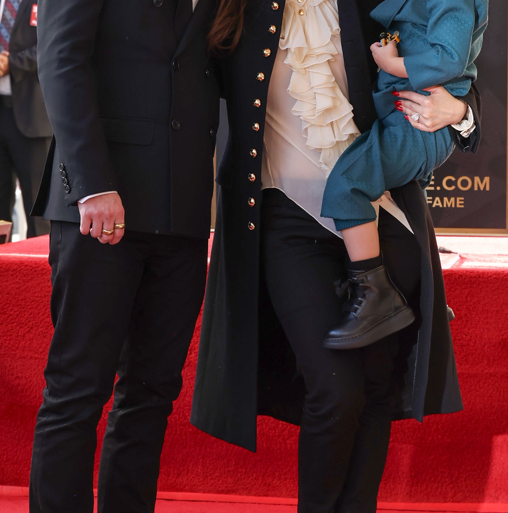 Macaulay Culkin and Brenda Song stand on a Hollywood Walk of Fame star with their child in their arms. Macaulay wears a suit, Brenda in long coat with frilled shirt