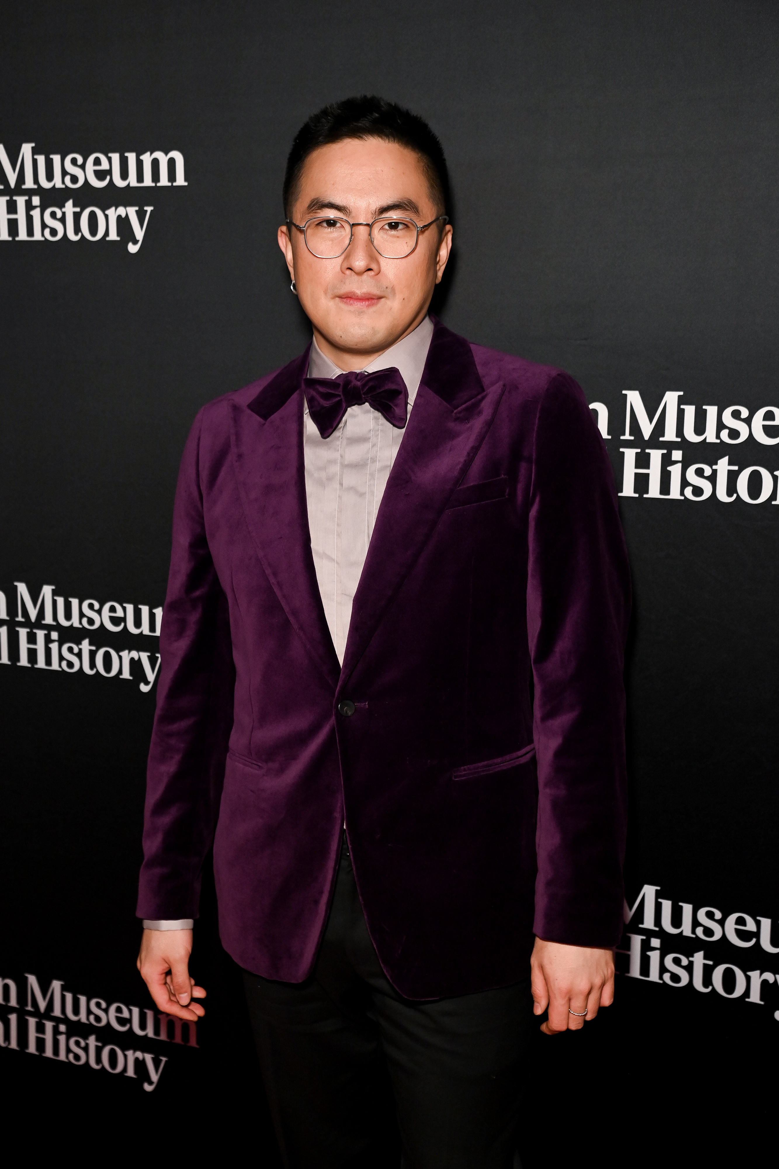 Bowen Yang in a purple velvet suit jacket, light-colored shirt, and bow tie at an event for the Museum of Natural History