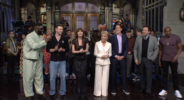 A group of people stand together on stage. Some wear casual clothing, others wear formal attire. Names of the individuals are unknown