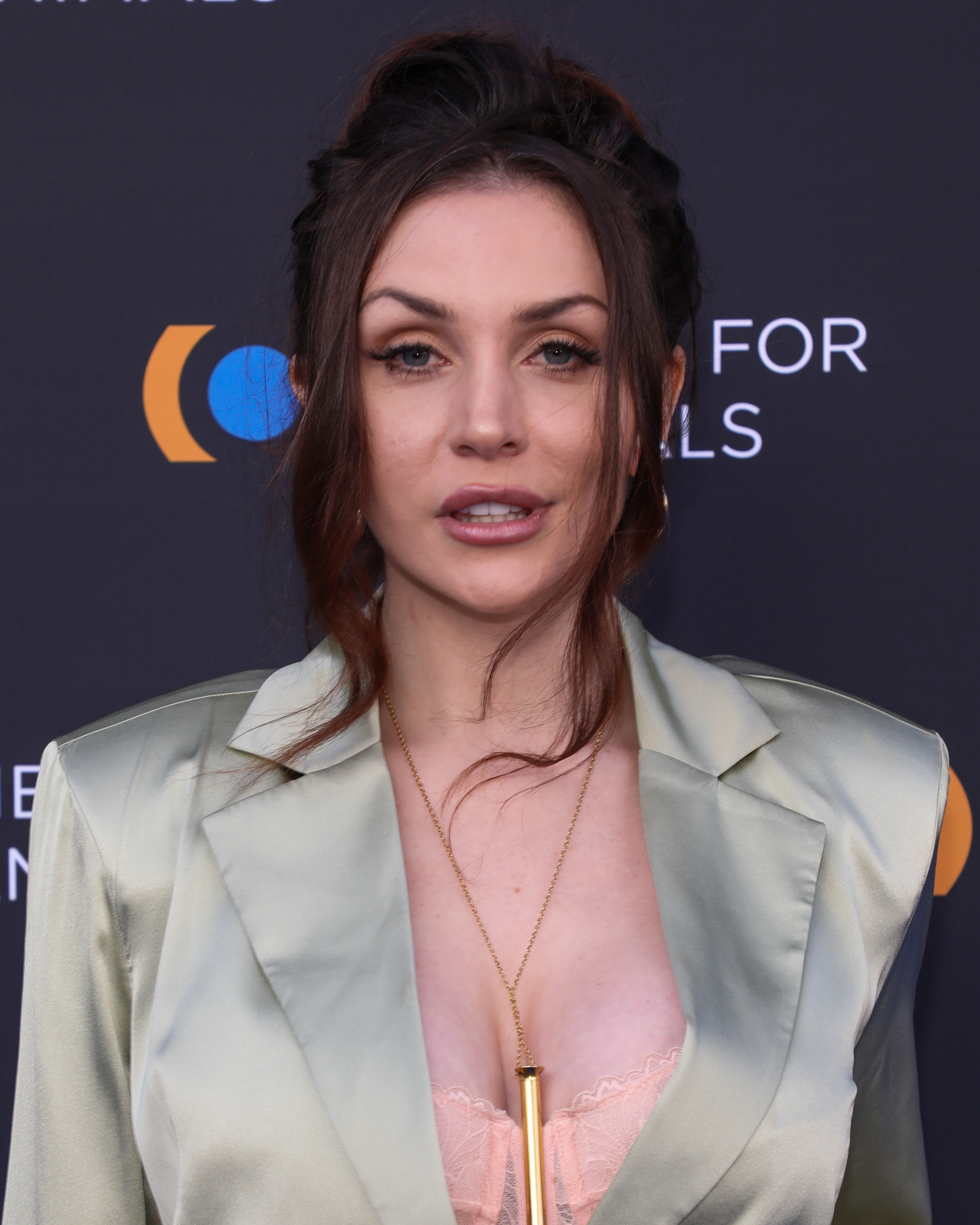 Courtney poses on the red carpet in a satin blazer with a long pendant necklace at an event