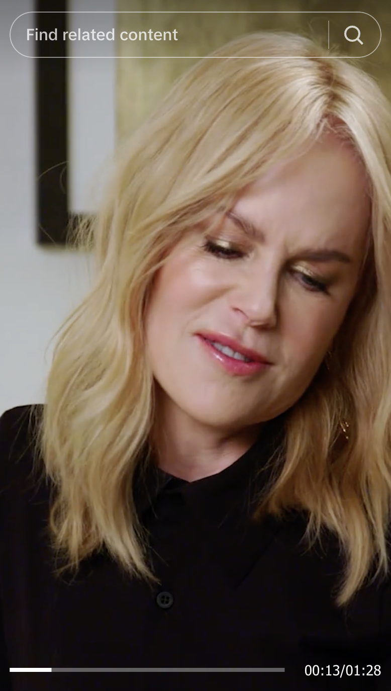 Nicole Kidman with shoulder-length wavy hair, wearing a black top, looking down thoughtfully
