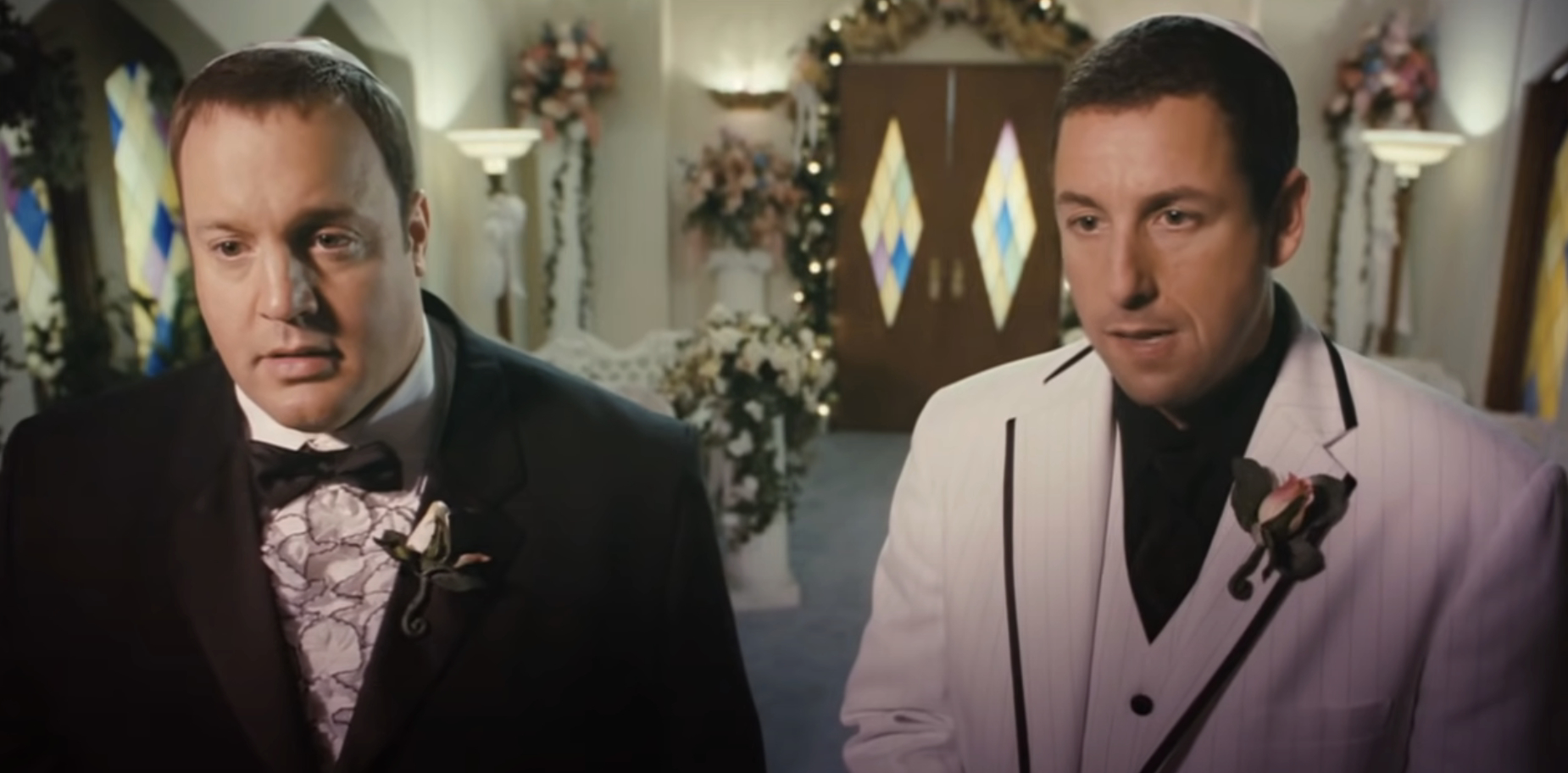 Kevin James in a black tuxedo and Adam Sandler in a white tuxedo stand in a decorated wedding venue scene from &quot;I Now Pronounce You Chuck And Larry&quot;