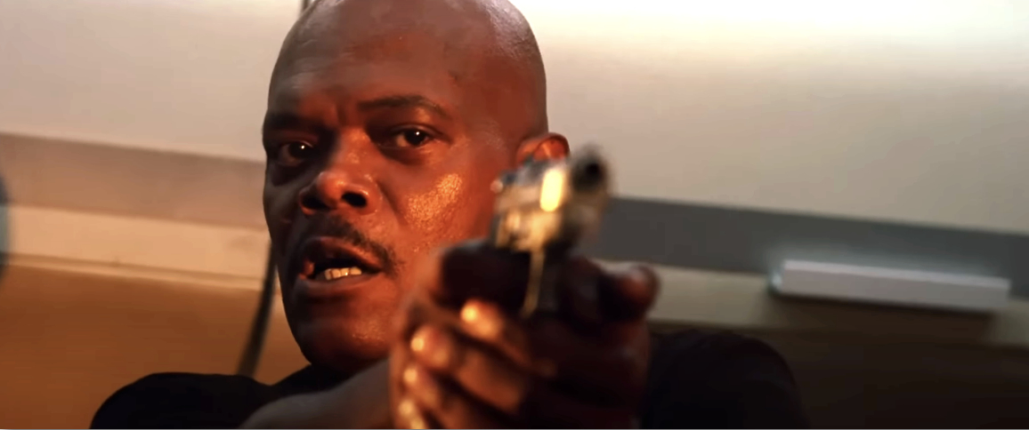 Samuel L. Jackson points a gun while looking intensely in a scene likely from a movie