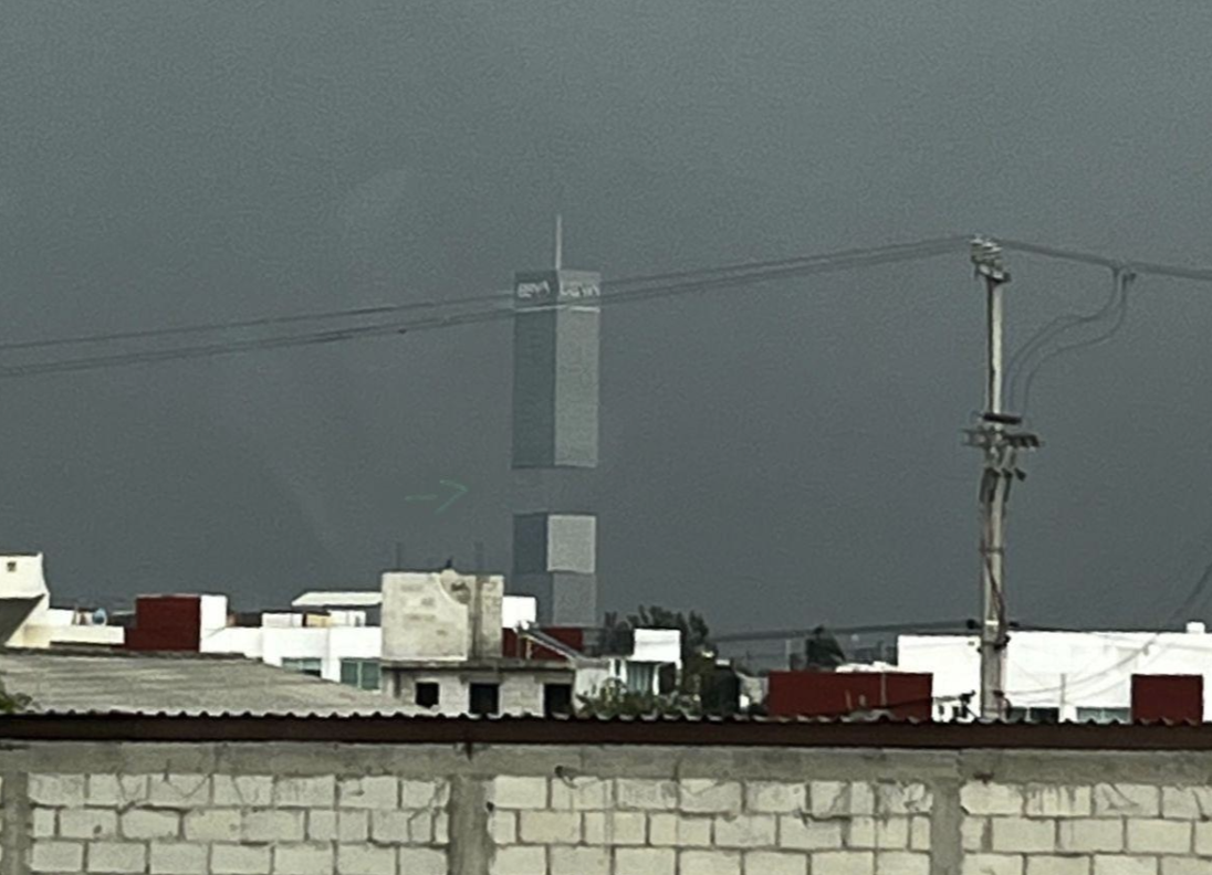Tall skyscraper standing above shorter buildings in front. There are utility poles and power lines in view