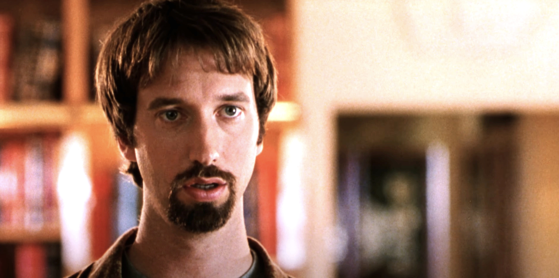 Tom Green in a still from a movie, looking forward with a neutral expression. He has short hair and a goatee