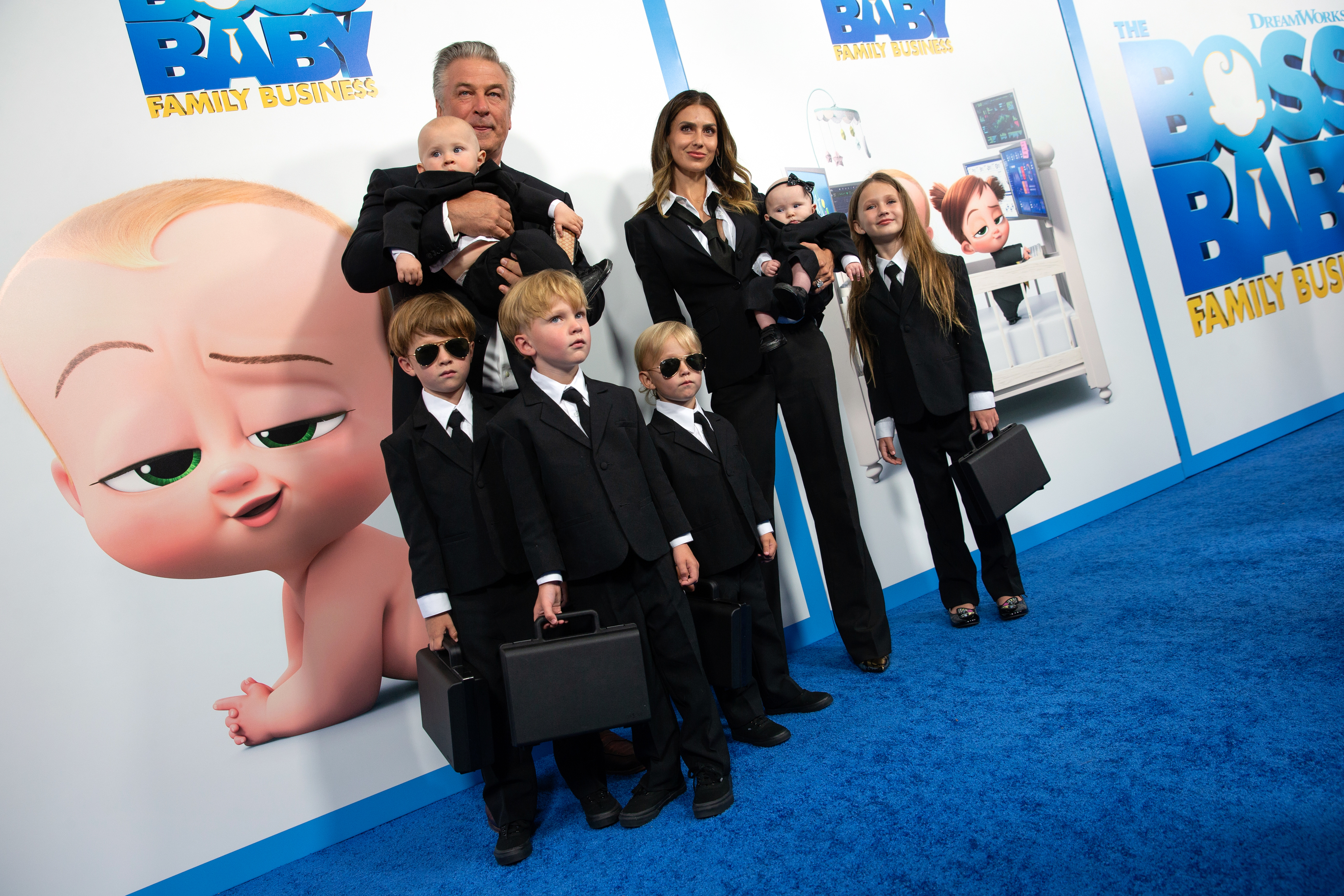 Alec Baldwin and Hilaria Baldwin stand with their children at the premiere of "The Boss Baby: Family Business," all dressed in black suits and holding briefcases