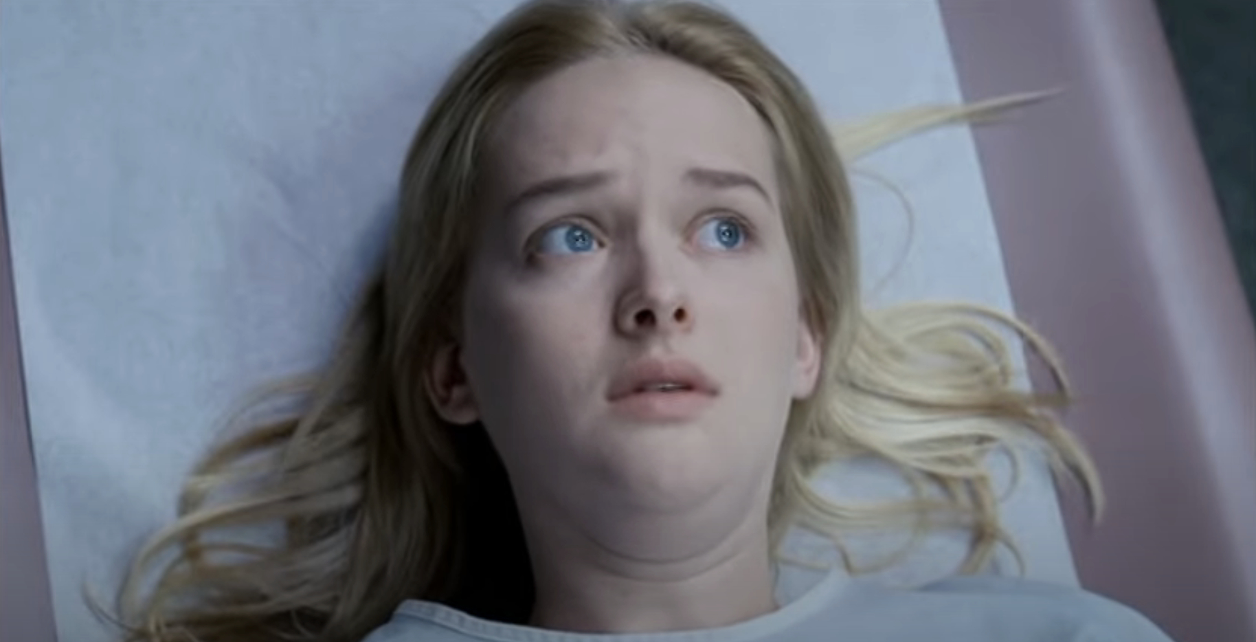 Joey King looking worried while lying on what seems like a medical examination table