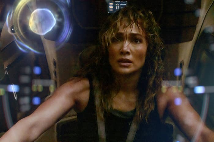 Jennifer Lopez, wearing a tank top, in a sci-fi scene, looks tense while operating a futuristic spaceship control panel
