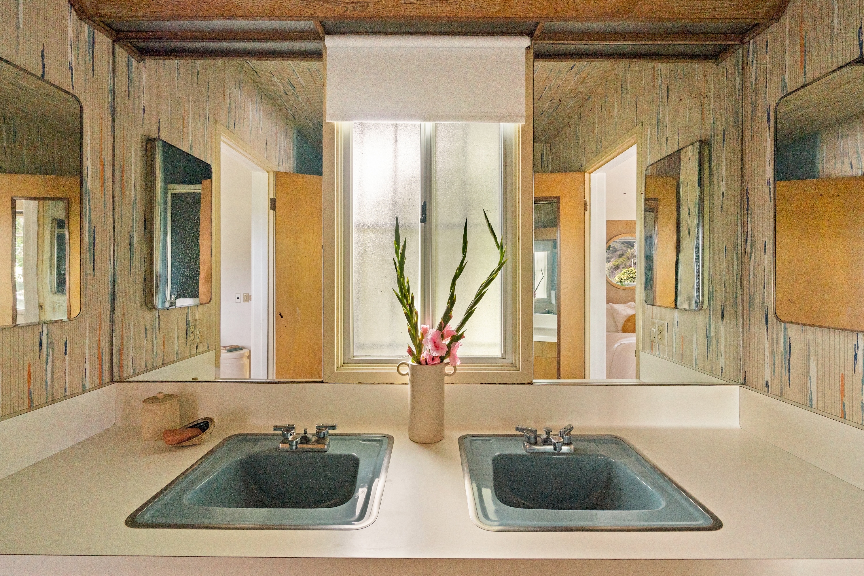 A stylish bathroom with double sinks and a mirrored vanity. A vase with flowers sits between the sinks