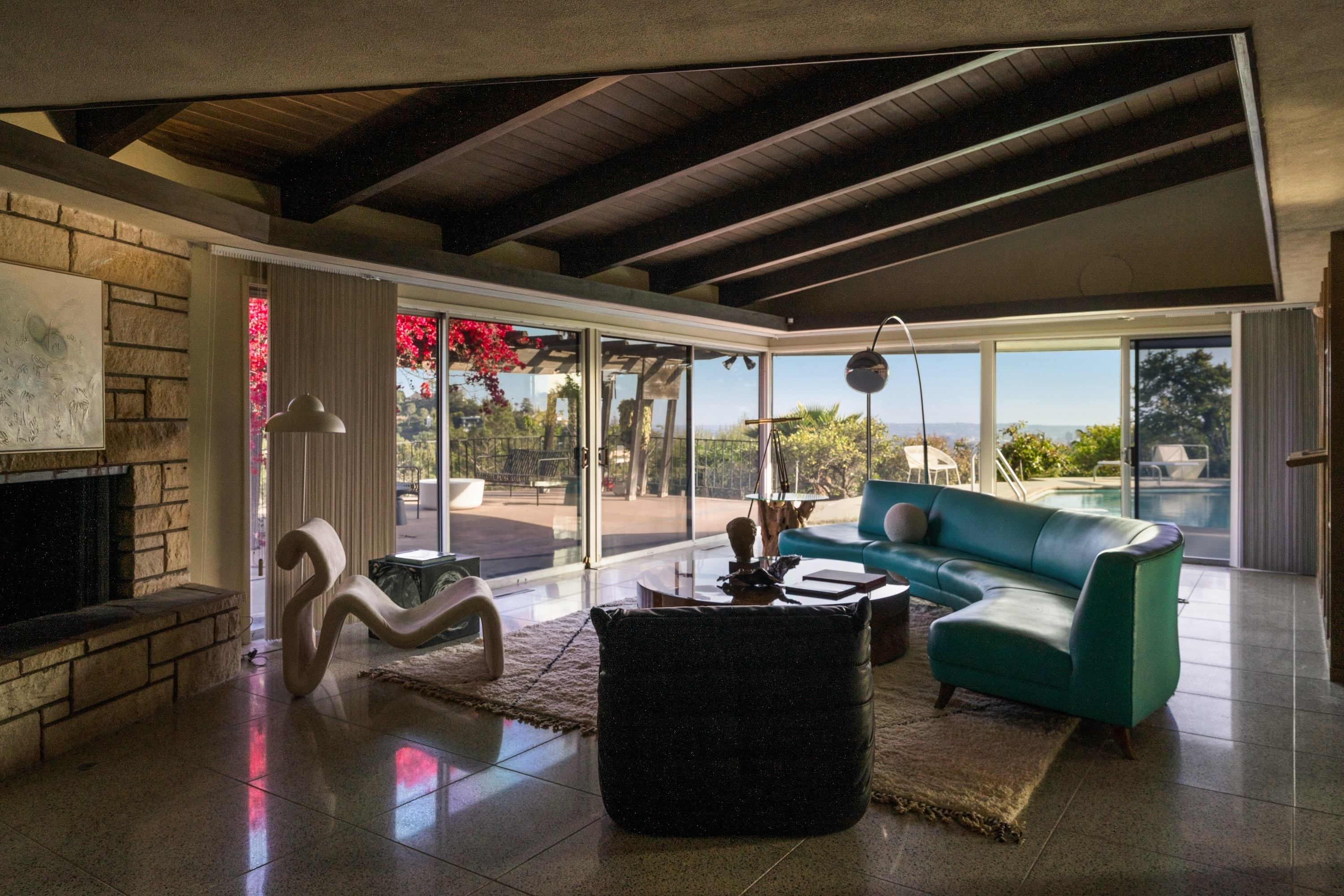 Mid-century modern living room with exposed beams, large windows, stylish furniture, and a pool view