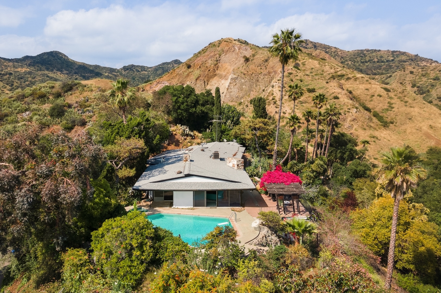 Aerial view of a house with a swimming pool nestled in a lush, mountainous landscape