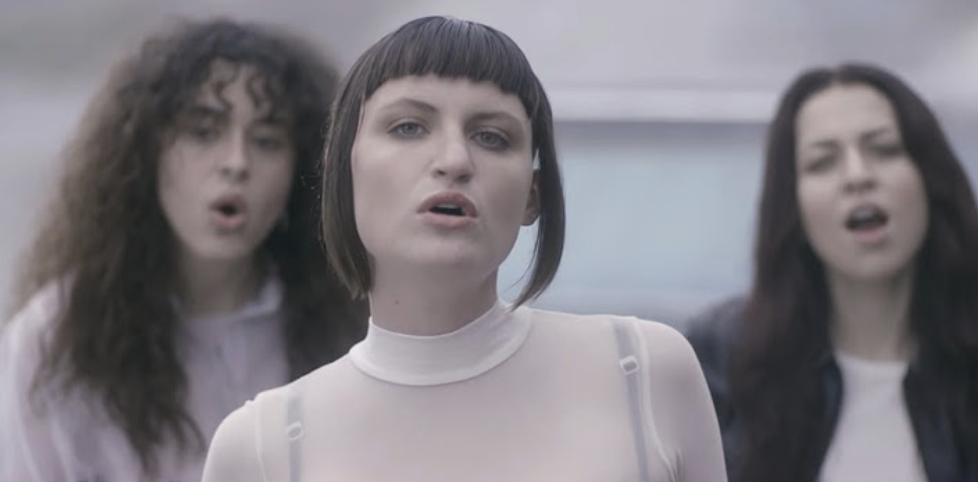 Rina Sawayama, HANA, and Shamir in sheer and casual attire, singing passionately together in an outdoor scene