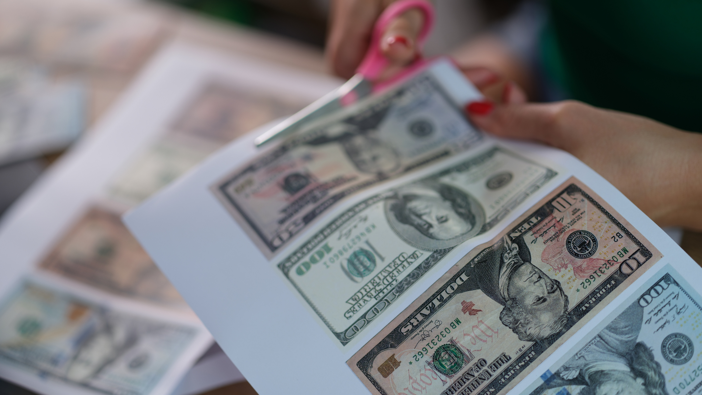 Hands holding scissors, cutting printed fake U.S. dollar bills
