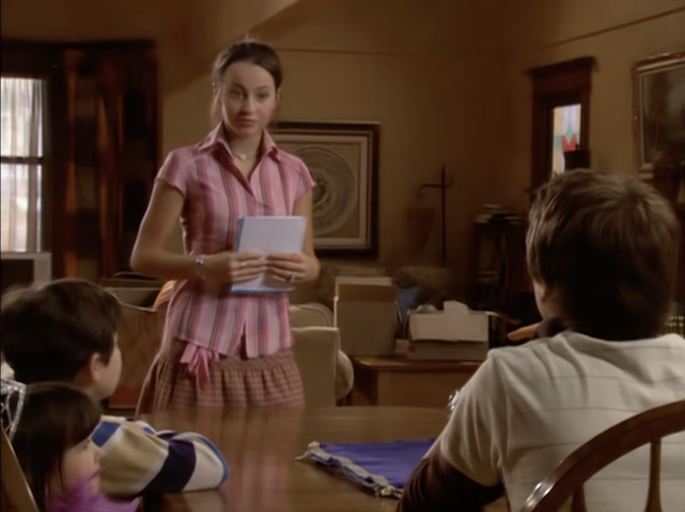 Woman stands holding papers while talking to children at a table