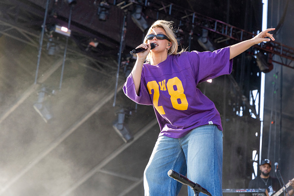 Reneé Rapp performs on stage wearing a loose jersey top with the number &quot;28&quot; and jeans