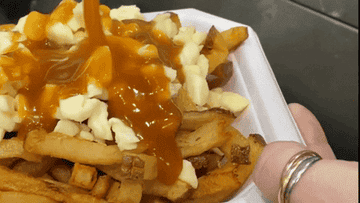 Close-up of poutine being prepared with fries, cheese curds, and gravy being poured on top