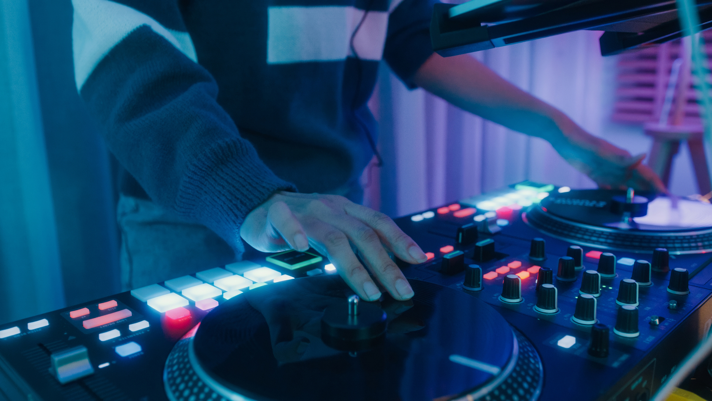 A DJ mixes music on a professional setup at a wedding. The image focuses on the DJ's hands and equipment