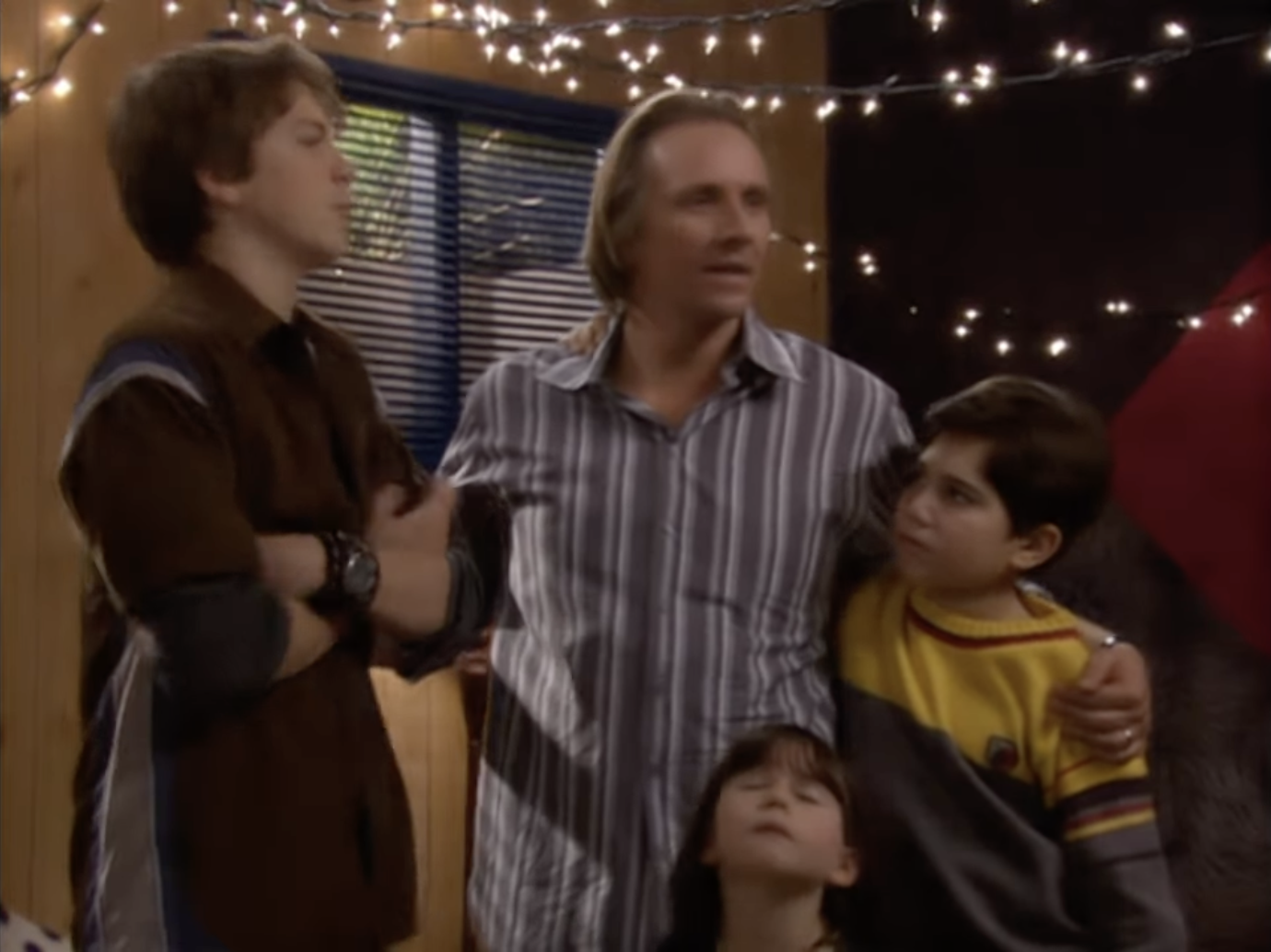 The image shows Jake Harper, Alan Harper, and Judith's new boyfriend Greg standing with Judith's kids Jake and Millie in a decorated room with string lights