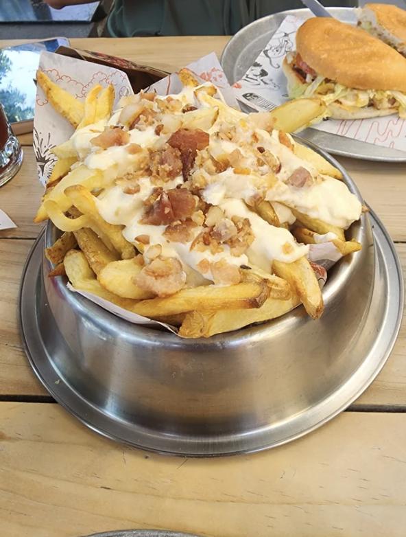 A plate of loaded fries topped with melted cheese and bacon bits, placed on a table alongside other food items