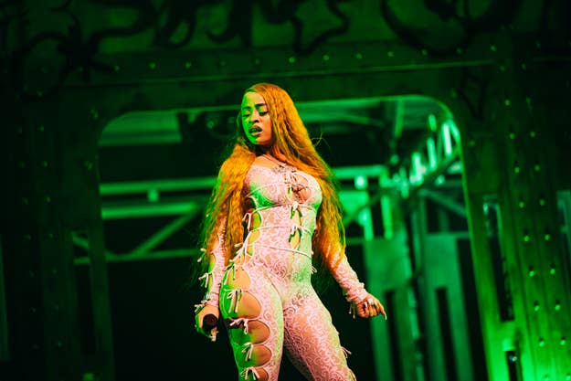 Rapper Ice Spice performs on stage in a revealing lace bodysuit with cut-out details and long hair flowing down, holding a microphone