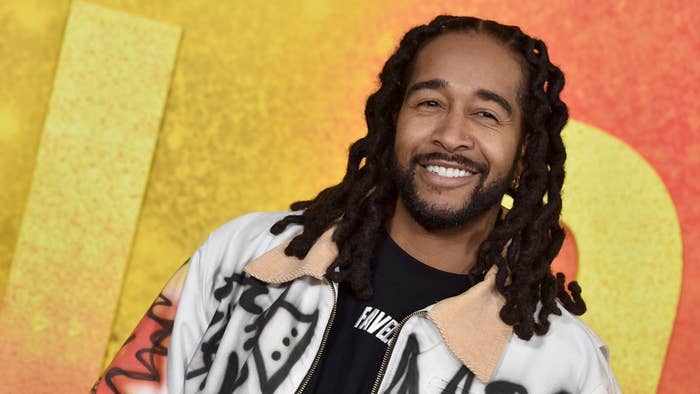Omarion smiles at an event, wearing a graffiti-style jacket over a black shirt