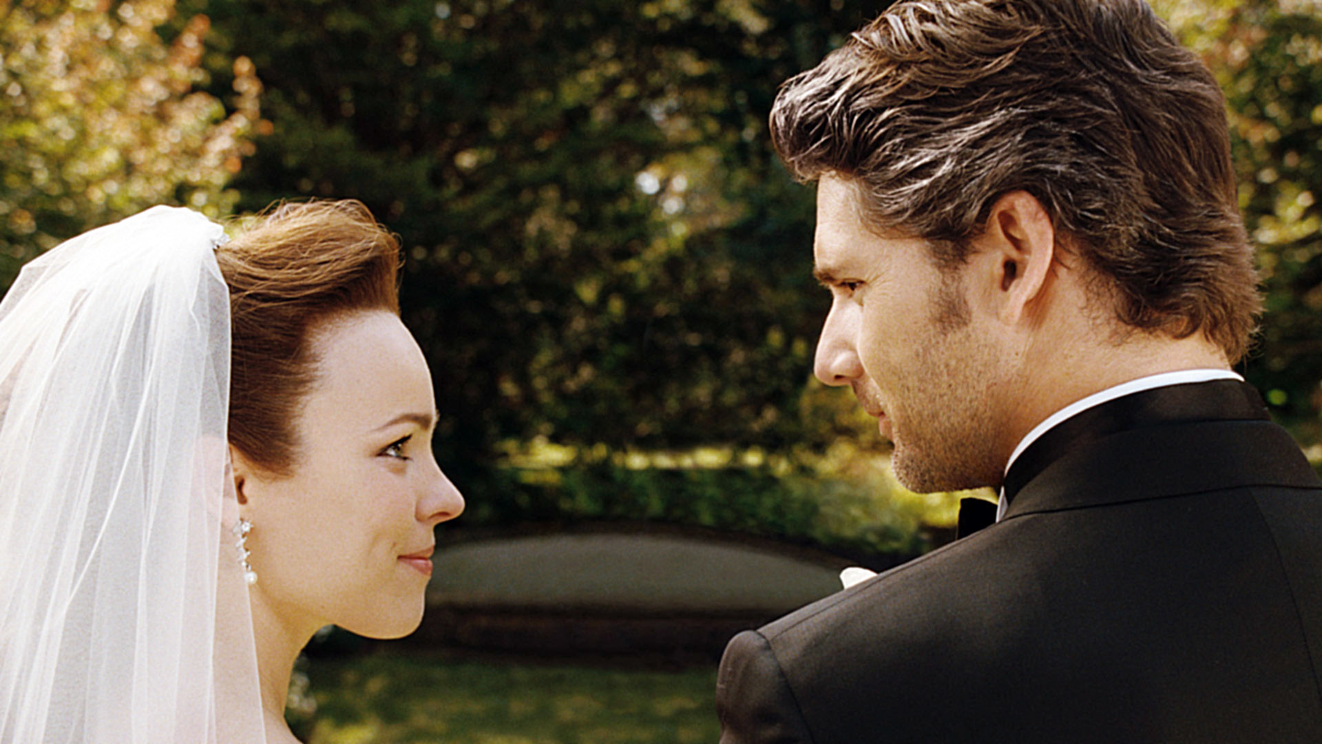 Rachel McAdams in a wedding dress and veil stares lovingly at Eric Bana in a tuxedo outdoors