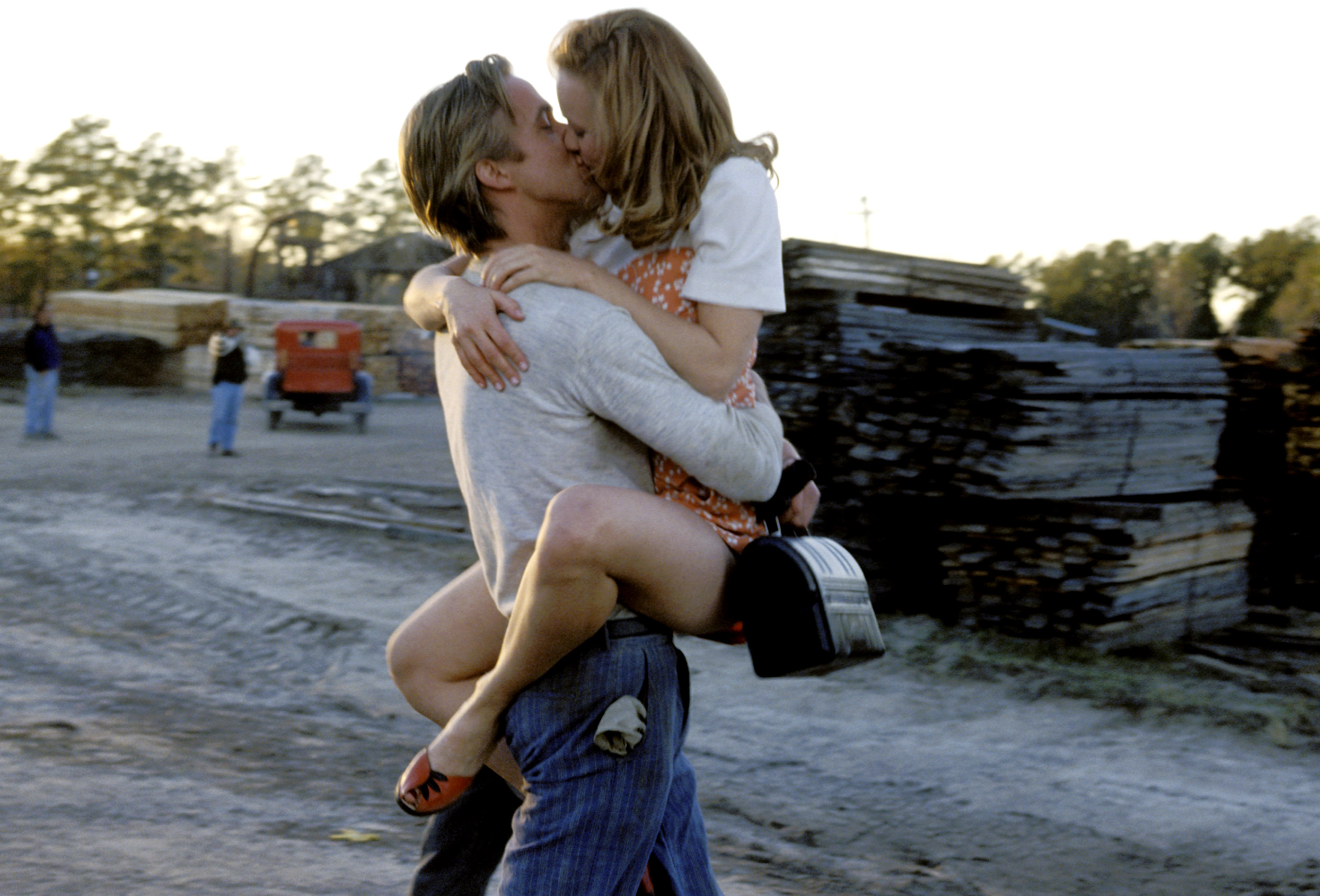 Ryan Gosling passionately lifts and kisses Rachel McAdams as she wraps her legs around him. They are in an outdoor, rural setting
