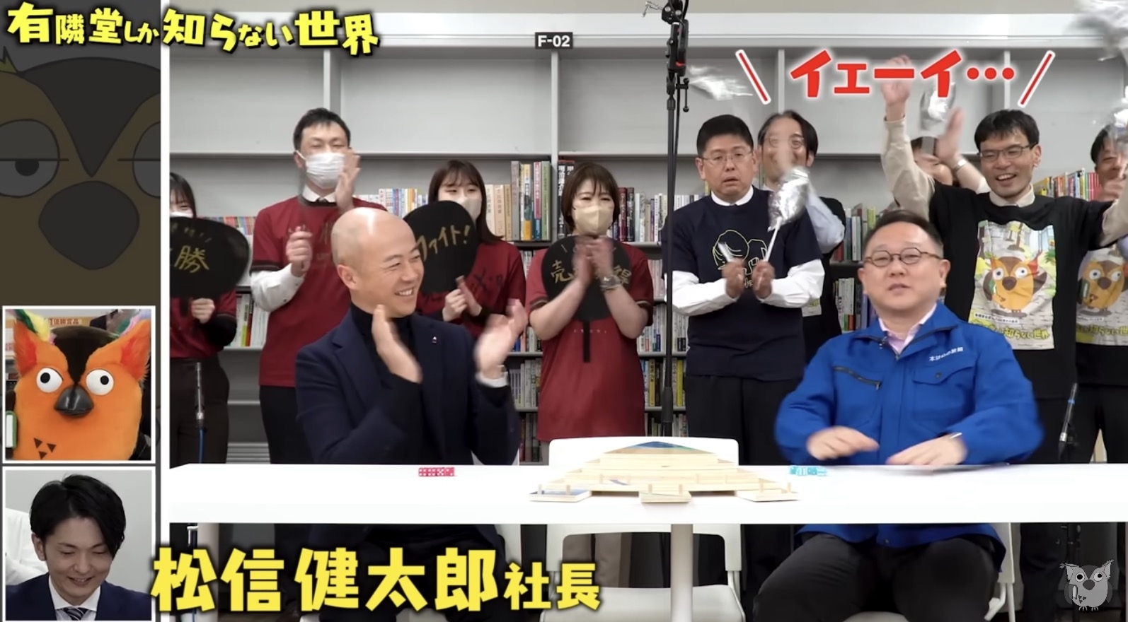 番組「有隣堂しか知らない世界」の一場面。松信健太朗社長がテーブルでインタビューを受けるシーン。周囲にはスタッフが拍手している。