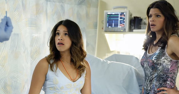 Gina Rodriguez and Andrea Navedo, in a hospital setting, look surprised as they face a person holding a medical tool