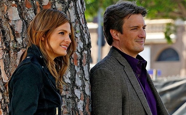 I don&#x27;t know who they are. Two people standing against a tree, smiling and looking ahead. The woman is wearing a jacket, and the man is in a blazer over a shirt