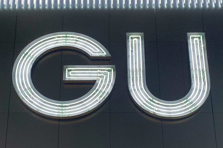 Illuminated sign with the letters &ldquo;GU&rdquo; mounted on a building, surrounded by vertical neon lights