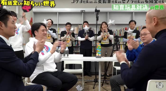 有隣堂しか知らない世界番組の撮影現場。複数の出演者が本棚の前で座って交流している。