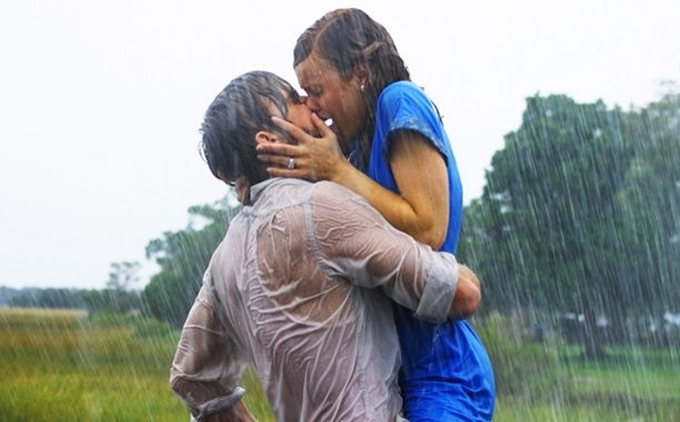 Ryan Gosling and Rachel McAdams passionately kiss in the rain, both soaked, recreating a famous scene from "The Notebook."