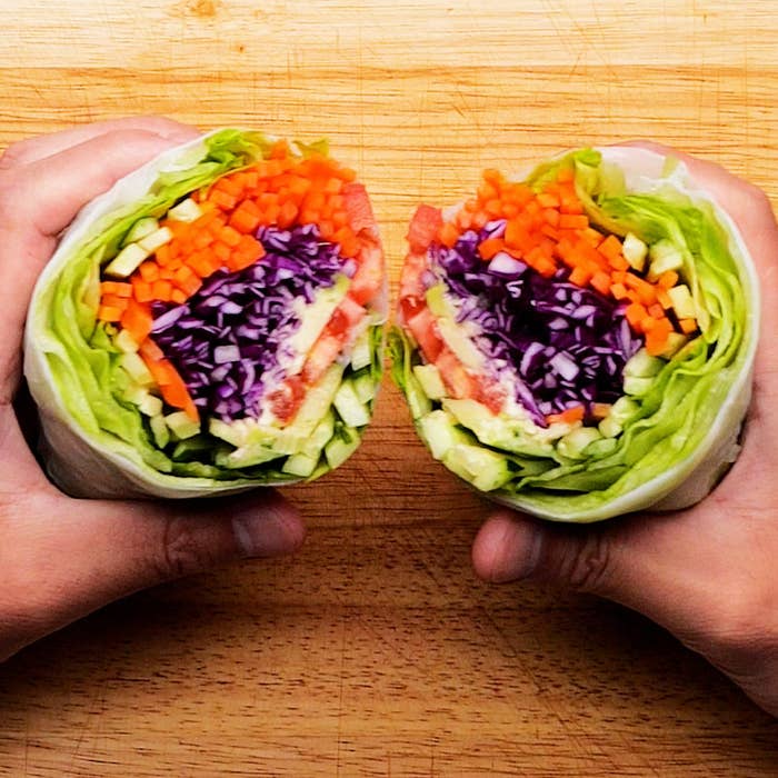 両手で持たれたラップサンドウィッチの断面。中にはレタス、にんじん、紫キャベツ、アボカドなどが詰まっています。