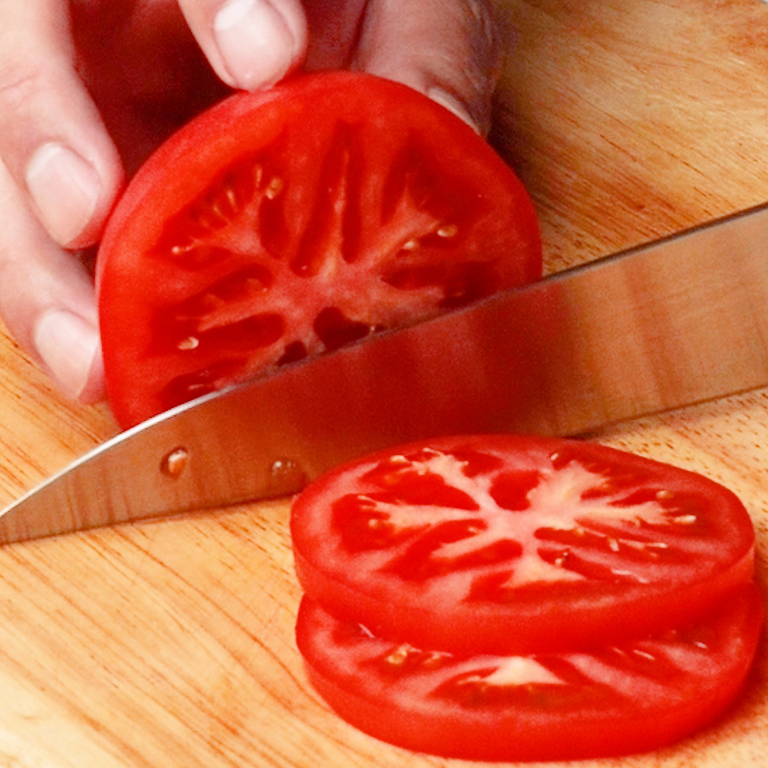 人の手がトマトを薄切りにしています。