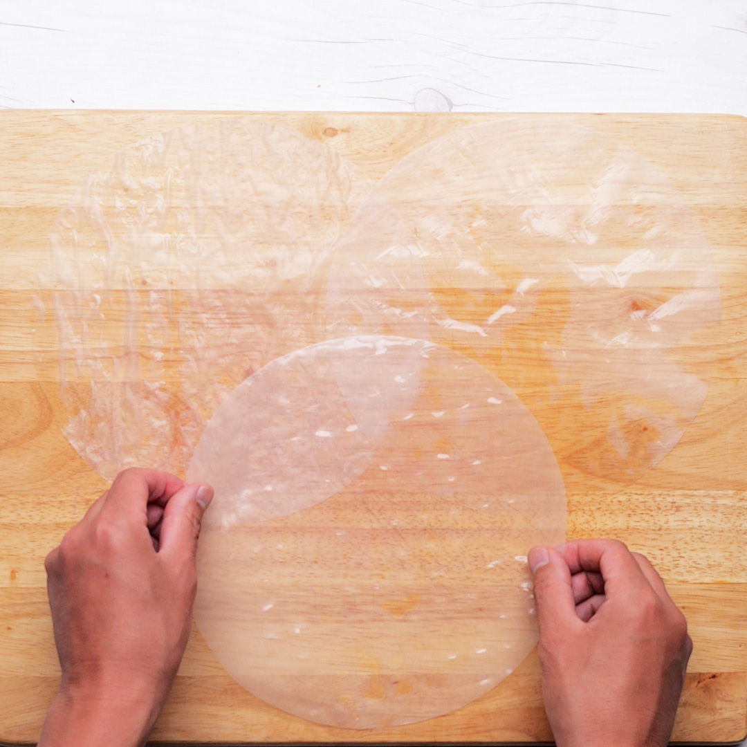 人がまな板の上でライスペーパーを扱っている様子。