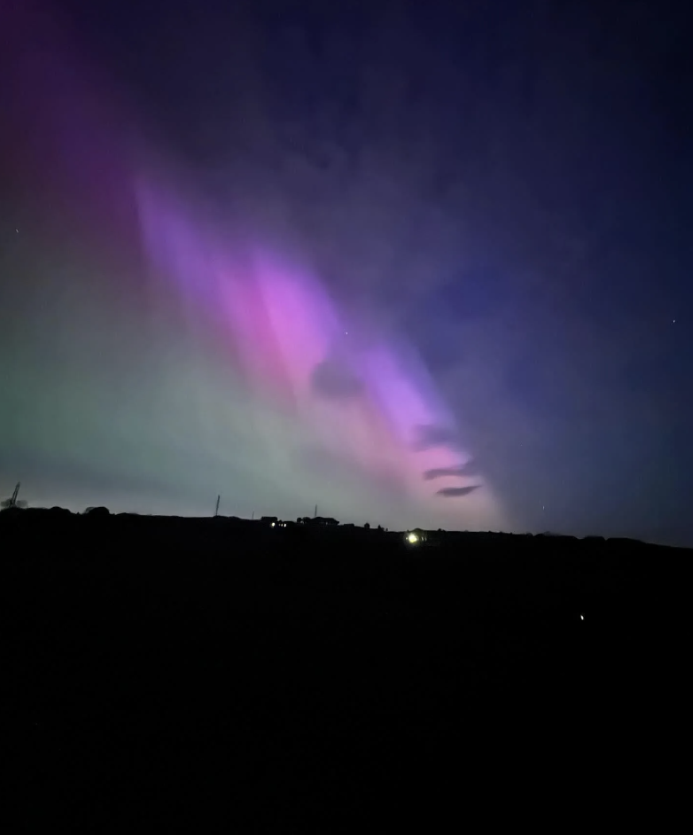 Night sky with a stunning display of aurora borealis (northern lights) in shades of purple and green over a silhouetted landscape