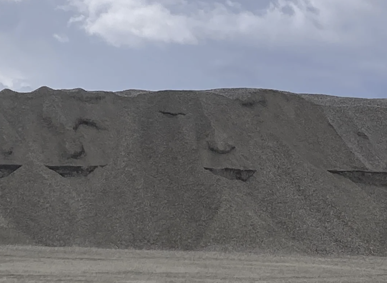 Large pile of gravel with indentations forming a smiley face under a cloudy sky