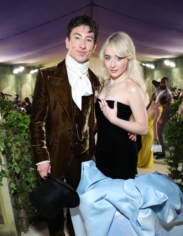 Barry Keoghan in a velvet suit and scarf with Sabrina Carpenter in a strapless gown with a dramatic train at a formal event