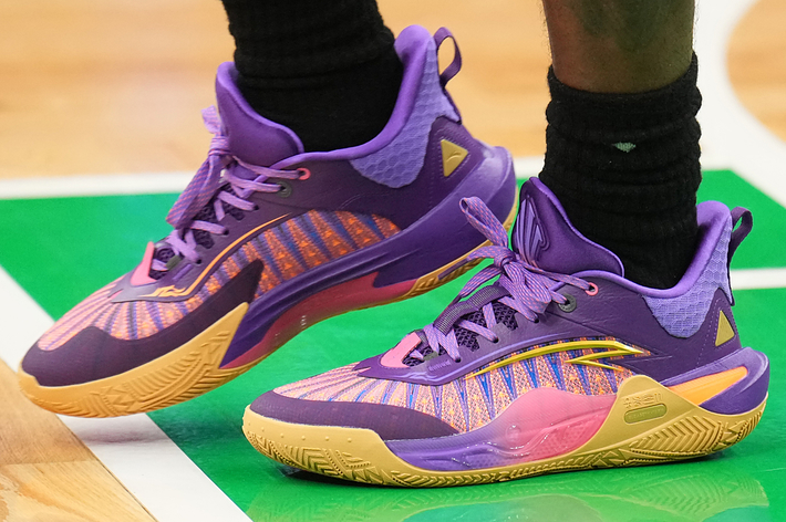 Person wearing purple and yellow athletic sneakers on a basketball court. Only the lower legs and feet are visible