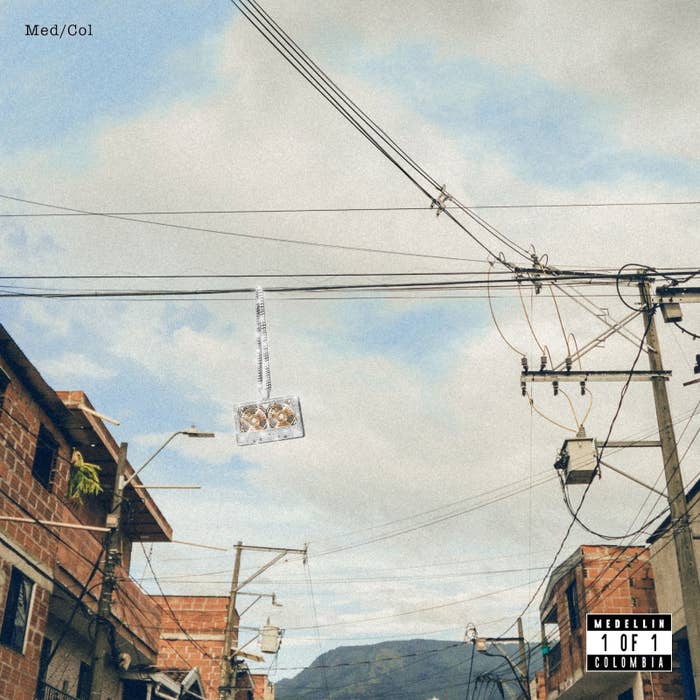 An image of utility poles and cables against a sky, with a diamond-studded cross pendant hanging amidst the wires. The image text reads &quot;Med/Col,&quot; &quot;Medellin,&quot; &quot;1 of 1,&quot; and &quot;Colombia.&quot;