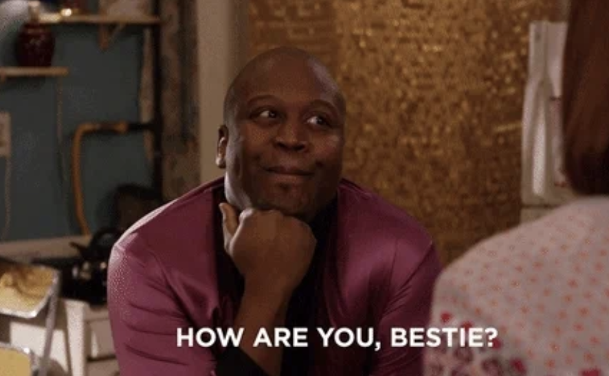 Tituss Burgess smiles and rests his chin on his hand with "HOW ARE YOU, BESTIE?" written at the bottom of the image