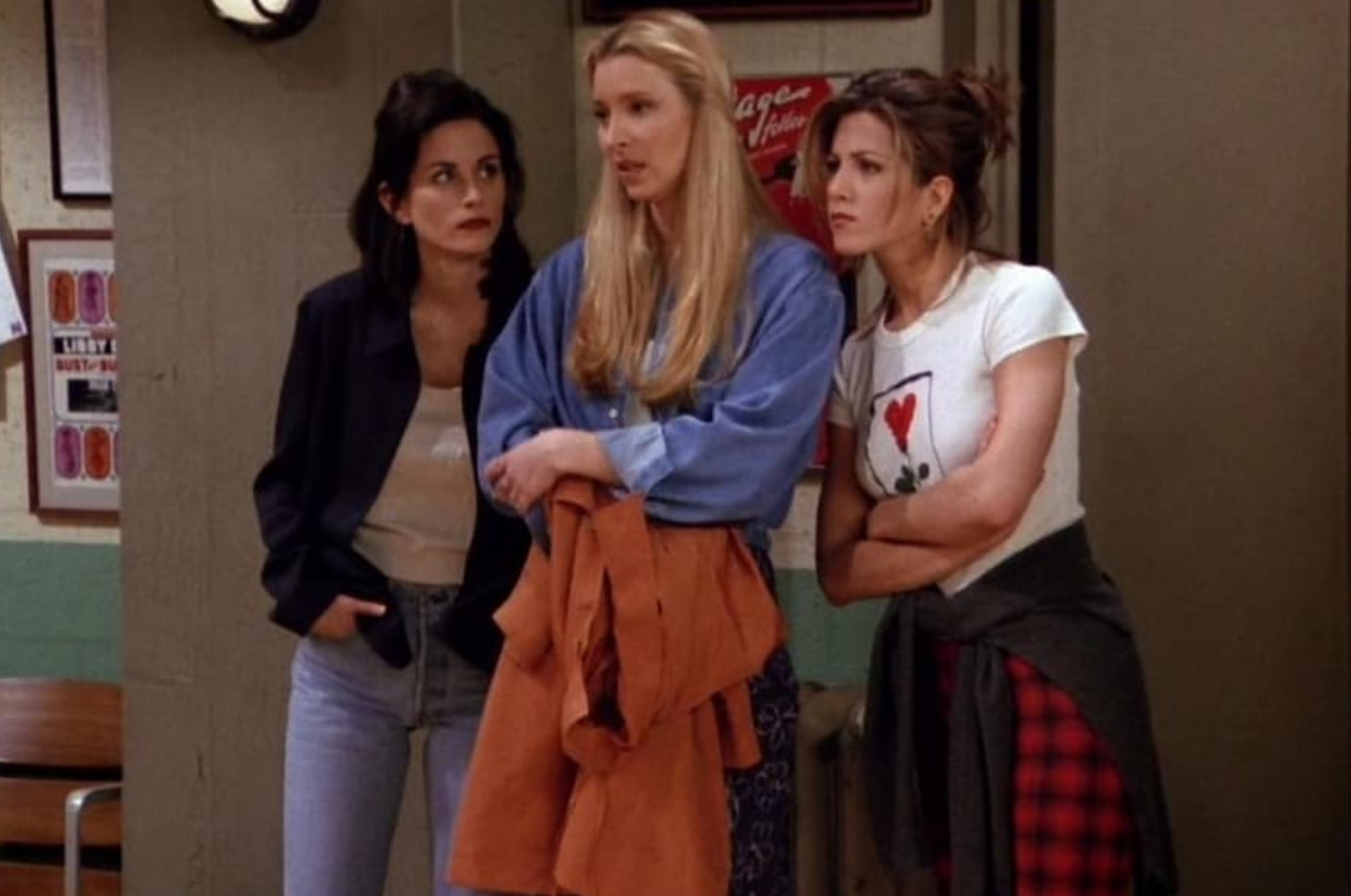 Courteney Cox, Lisa Kudrow, and Jennifer Aniston stand together, looking concerned. They are dressed casually