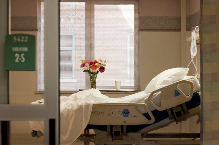 Hospital room with an empty bed, fresh flowers in a vase, and an IV stand near the bed