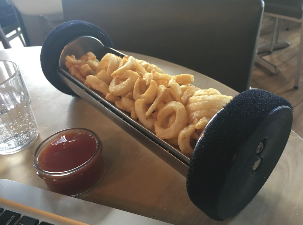 A unique cat toy wand filled with curly fries is placed on a table next to a small bowl of ketchup and a glass of water
