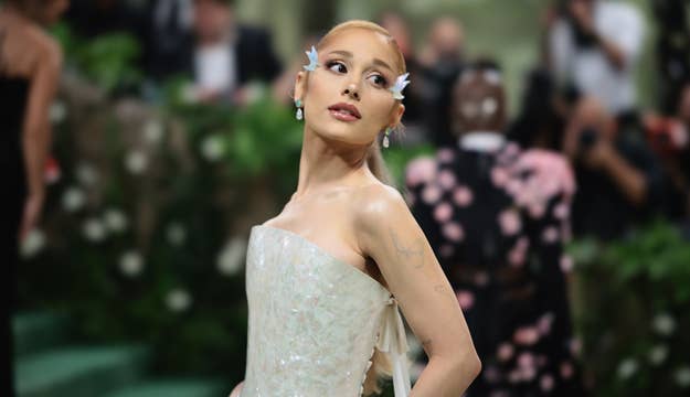 Ariana Grande poses in an elegant strapless gown adorned with floral appliques at a formal event. She wears white flower accessories in her hair