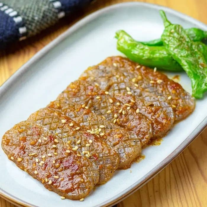 皿に切られたコンニャクのステーキと付け合わせの焼きししとうが載っている。