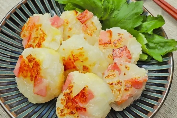 皿に盛られたポテトチーズ焼きと葉物野菜が飾られた料理。右上に箸と箸置きがある。