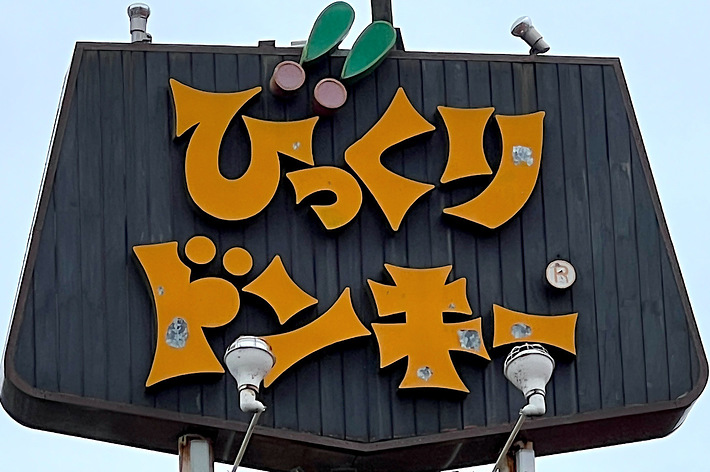 A large sign with Japanese text and a stylized cartoon character on top. The text reads “びっくり ドンキー,” translating to “Bikkuri Donkey."